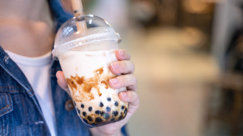 Young Woman Is Holding, Drinking Brown Sugar Flavored Tapioca Pearl Bubble Milk Tea With Glass Straw In Night Market Of Taiwan, Close Up, Bokeh