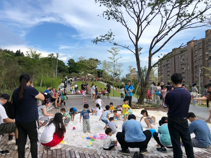 大有梯田生態公園內的白沙坑遊戲區，孩子們在沙地玩耍，家長坐在草坡旁陪伴
