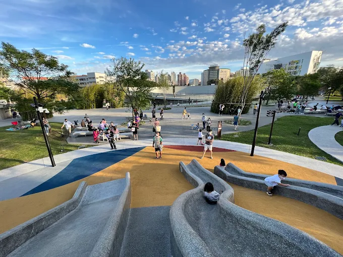 復興親子公園內三道滑梯與廣場設計，小朋友在磨石溜滑梯上玩耍，家長坐在周圍休憩
