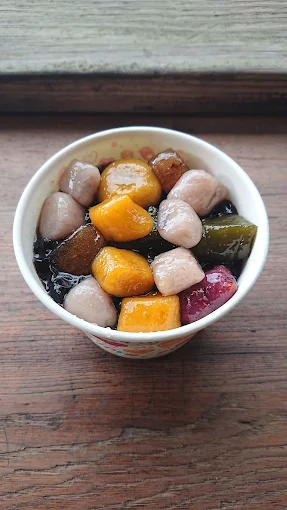 刨冰上覆蓋各式芋圓、粉粿與仙草，擺放在木桌上
