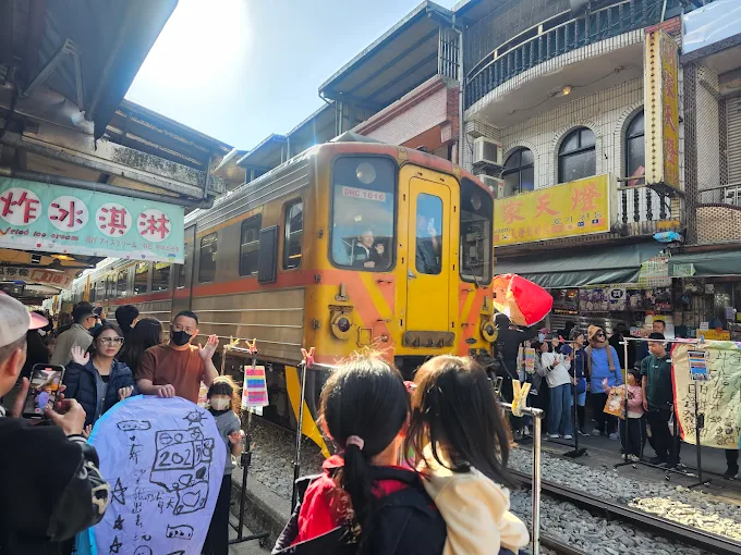 台鐵列車緩慢通過平溪老街，旅客圍觀並放飛天燈，街道洋溢節慶氛圍
