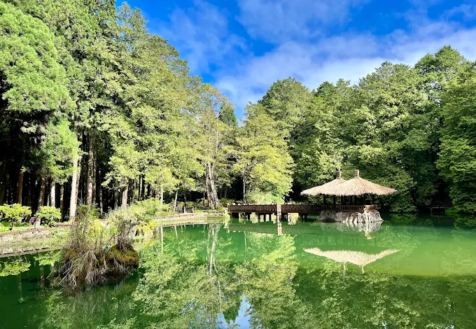 阿里山姊妹潭碧綠湖水倒映藍天與樹林，湖中有木造涼亭與小島