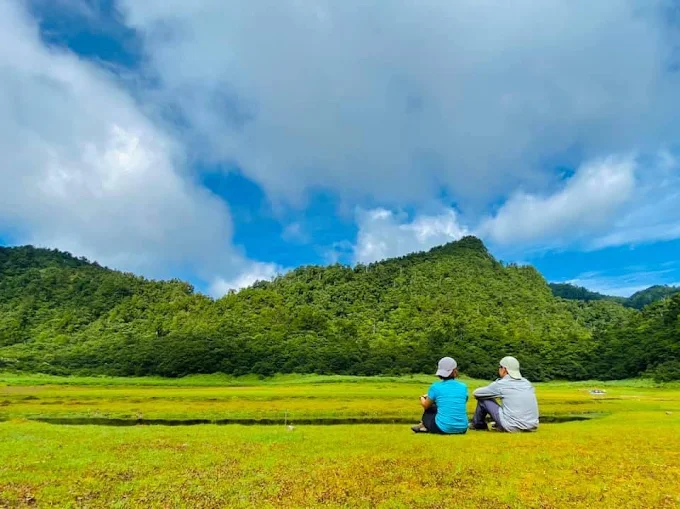 兩位登山客坐在松蘿湖草地上,遠眺群山與湖泊,享受靜謐自然景色