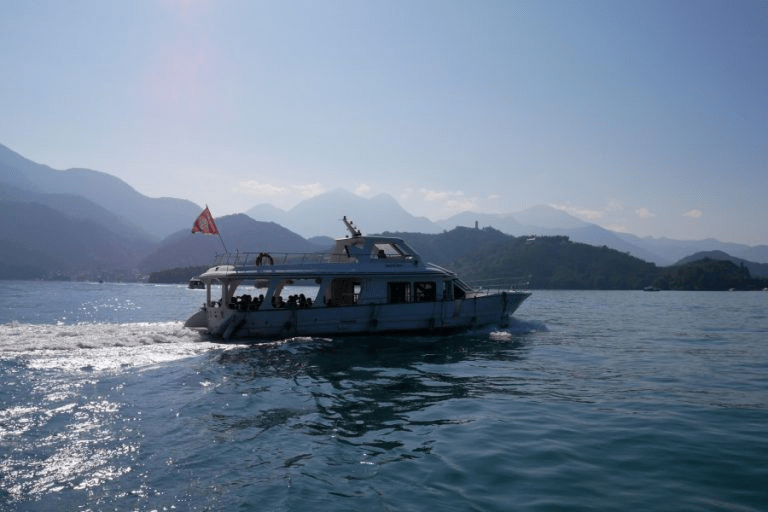 白色的遊艇行駛在碧綠的日月潭湖面上，背景是層疊的青山