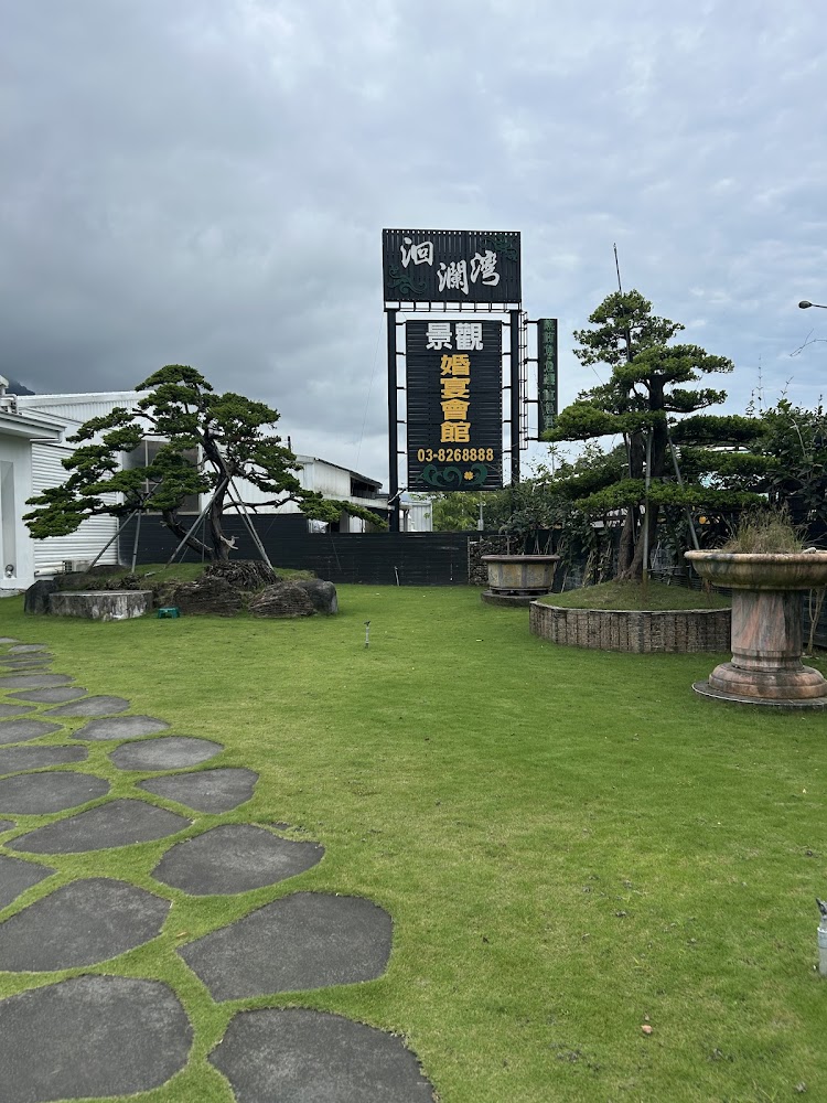 洄瀾灣園區草地與石板步道，前方有大型婚宴會館招牌與整齊樹木