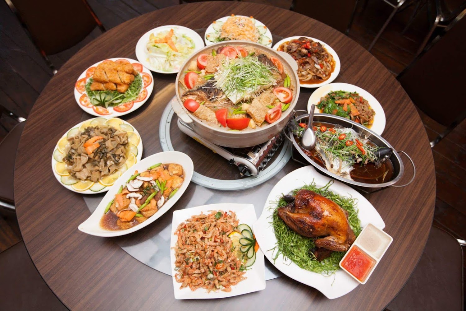 一桌豐盛中式合菜，有火鍋、烤雞、蒸魚、蝦與青菜