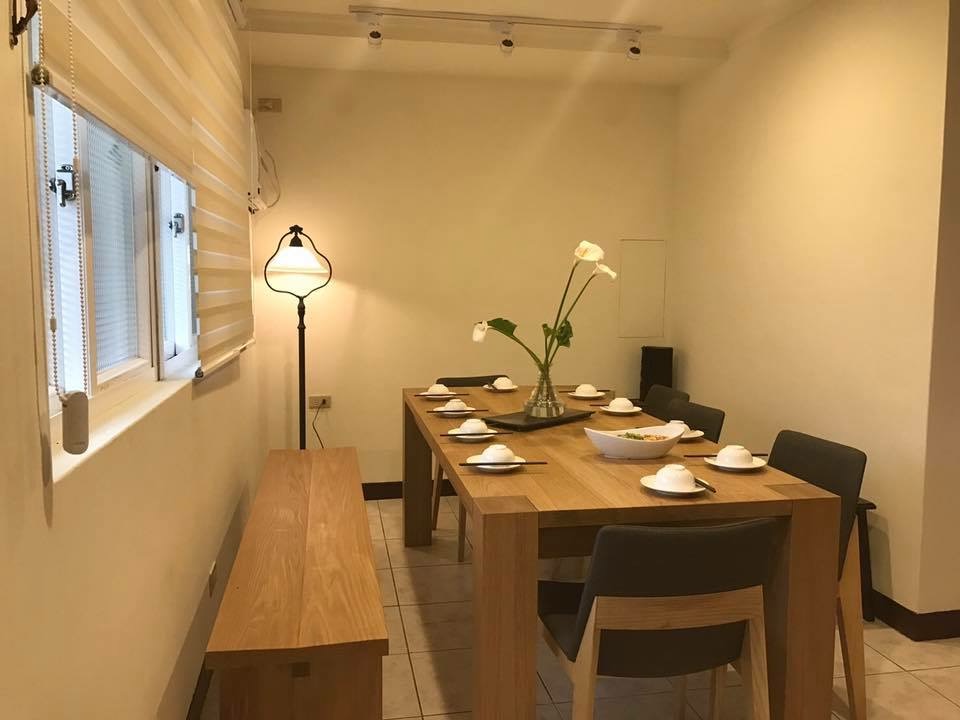這是一間簡約風格的餐廳，有一張木質餐桌、數把椅子和一張長凳，桌上擺放著餐具和花藝裝飾，角落有落地燈，環境溫馨整潔。