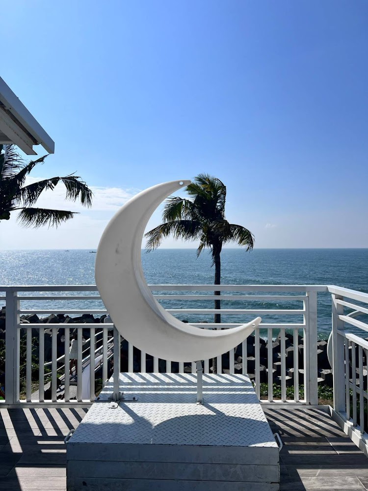 愛琴海岸海景渡假農場露營區的戶外陽台，有大型白色新月裝置，背景為海景與椰子樹。