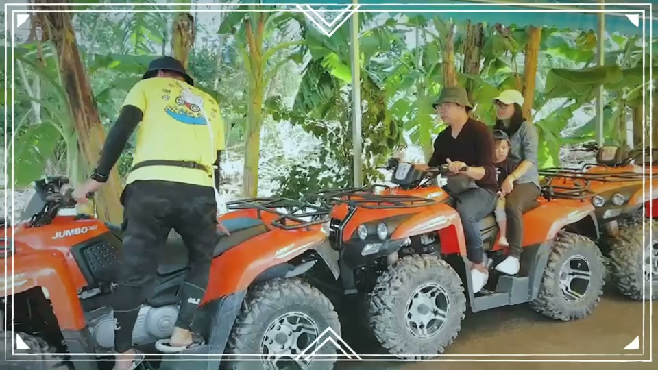 這張圖片中有數輛橘色的越野沙灘車,畫面右邊有三人騎乘同一輛車,旁邊有一位穿著黃色背心的工作人員正在協助。背景為綠色的樹林和棚子,無明顯浮水印。