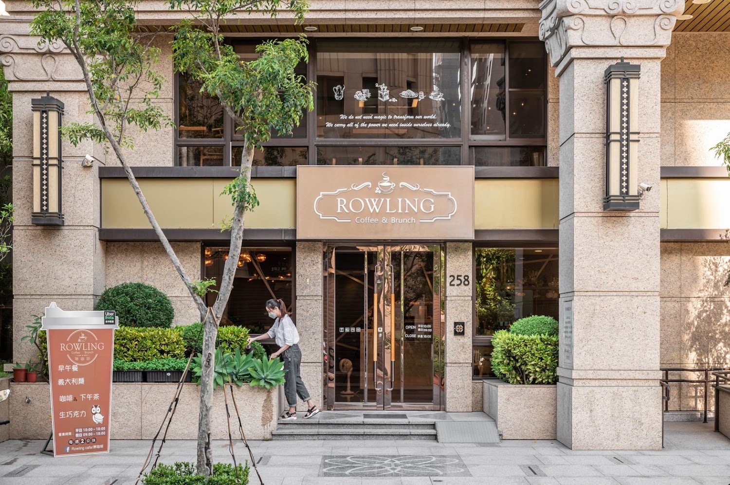 這是一家名為ROWLING的咖啡早午餐店，店門口有植物、招牌、玻璃門和營業時間告示，一位女子站在門前整理綠植，環境看起來整潔舒適。