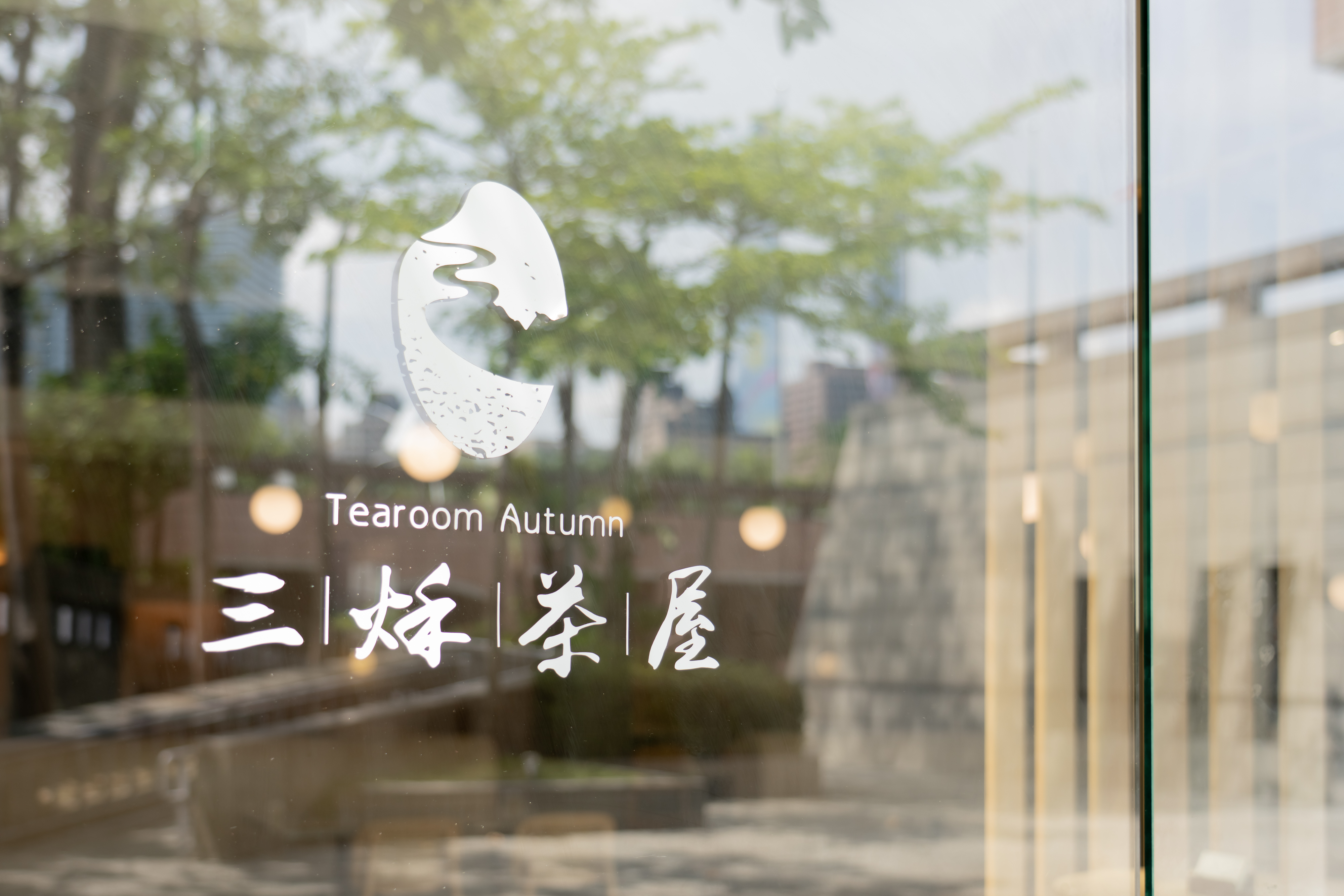 這張圖片主要是玻璃門上的店家標誌，寫有『三好茶屋 Tearoom Autumn』，旁邊有一個造型簡約的茶葉圖案，背景則是戶外街景和樹木。
