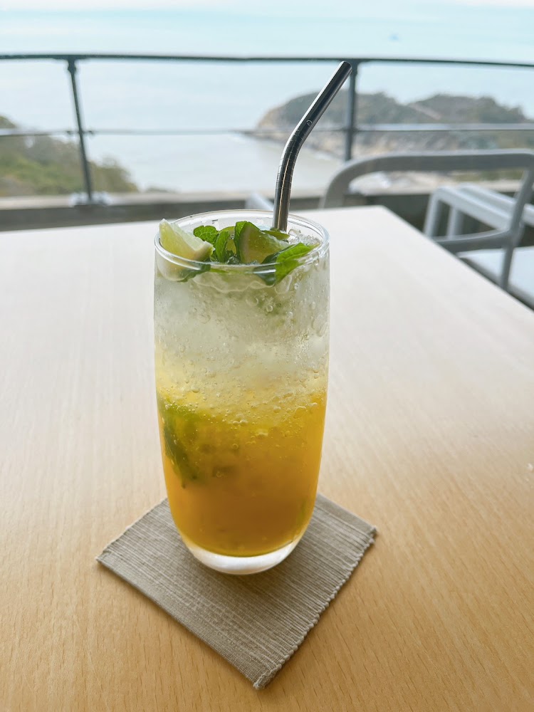 高腳杯中有薄荷葉、檸檬片和碎冰的清爽飲料，背景是海景與戶外座椅