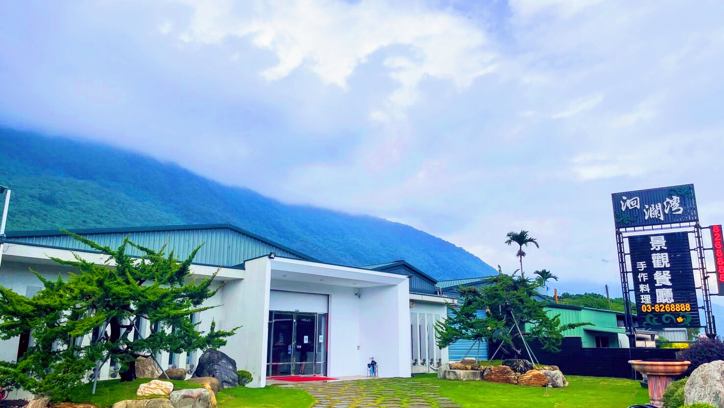 山腳下的洄瀾灣景觀餐廳外觀，建築明亮現代，背景有雲霧山景
