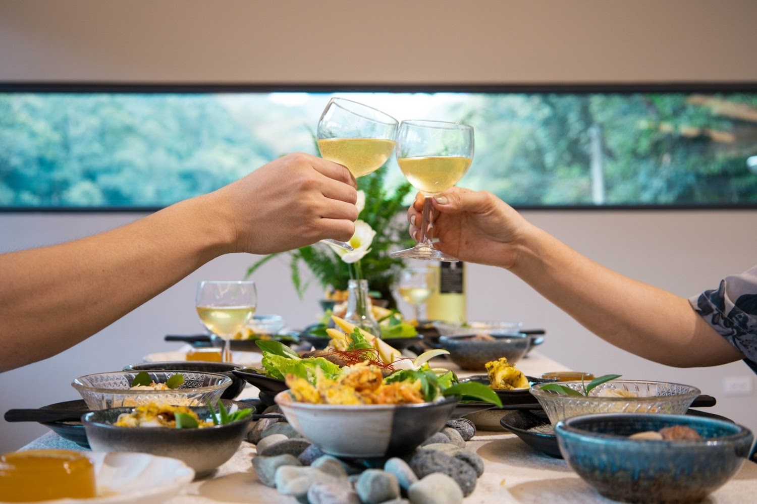 兩人在窗邊餐桌前舉杯與多道料理