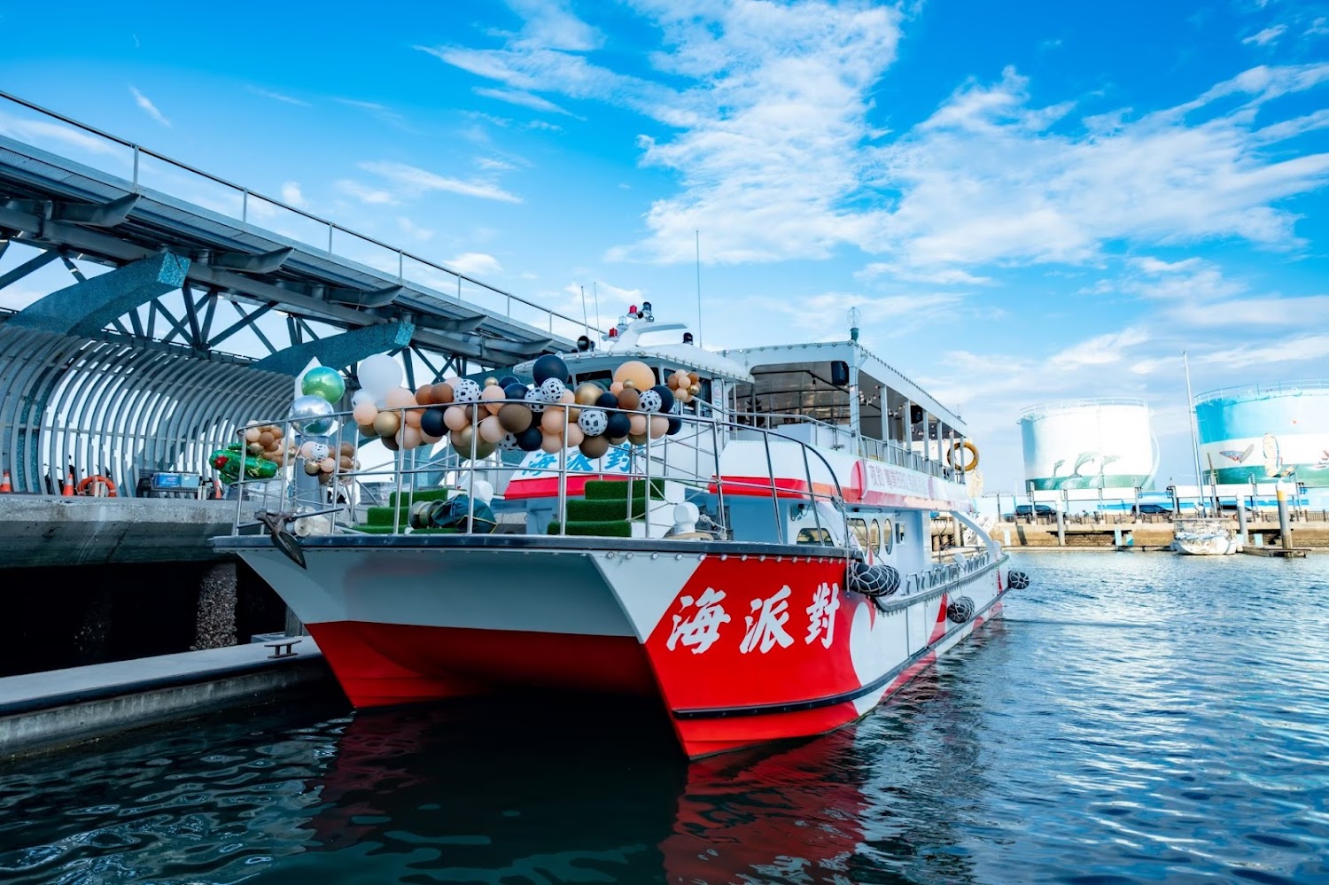 港口邊停著裝飾氣球的派對船，天氣晴朗。