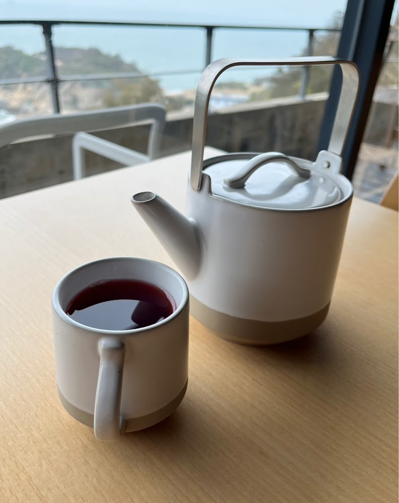 白色壺和深紅飲品馬克杯擺在桌上，背景是壯麗山景