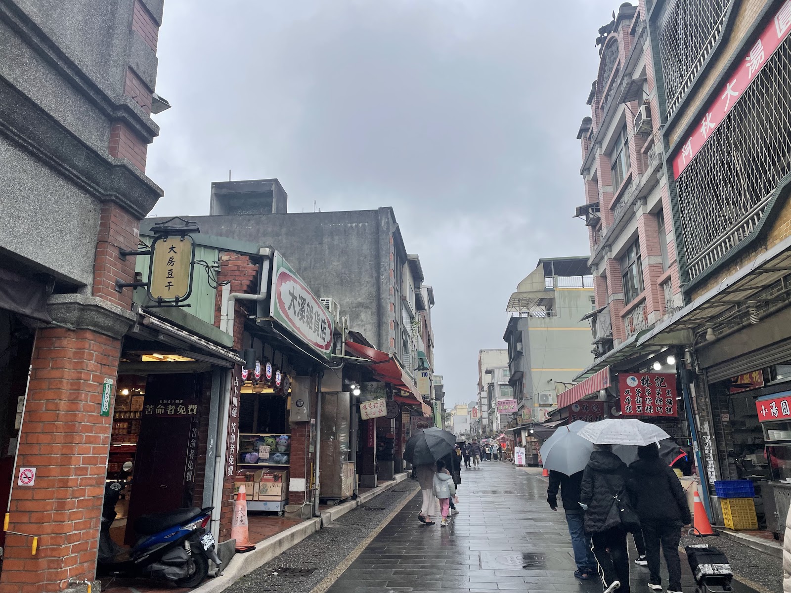 大溪老街雨天街景，兩側傳統閩南商家林立，行人撐傘漫步