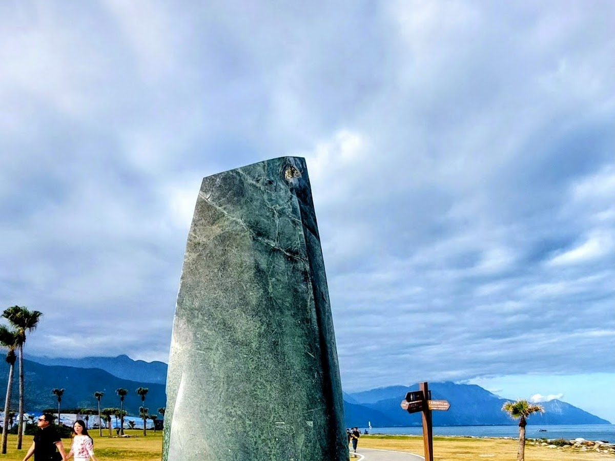 七星潭海灘大型黑色花崗岩石柱雕塑，背景山脈海洋藍天白雲