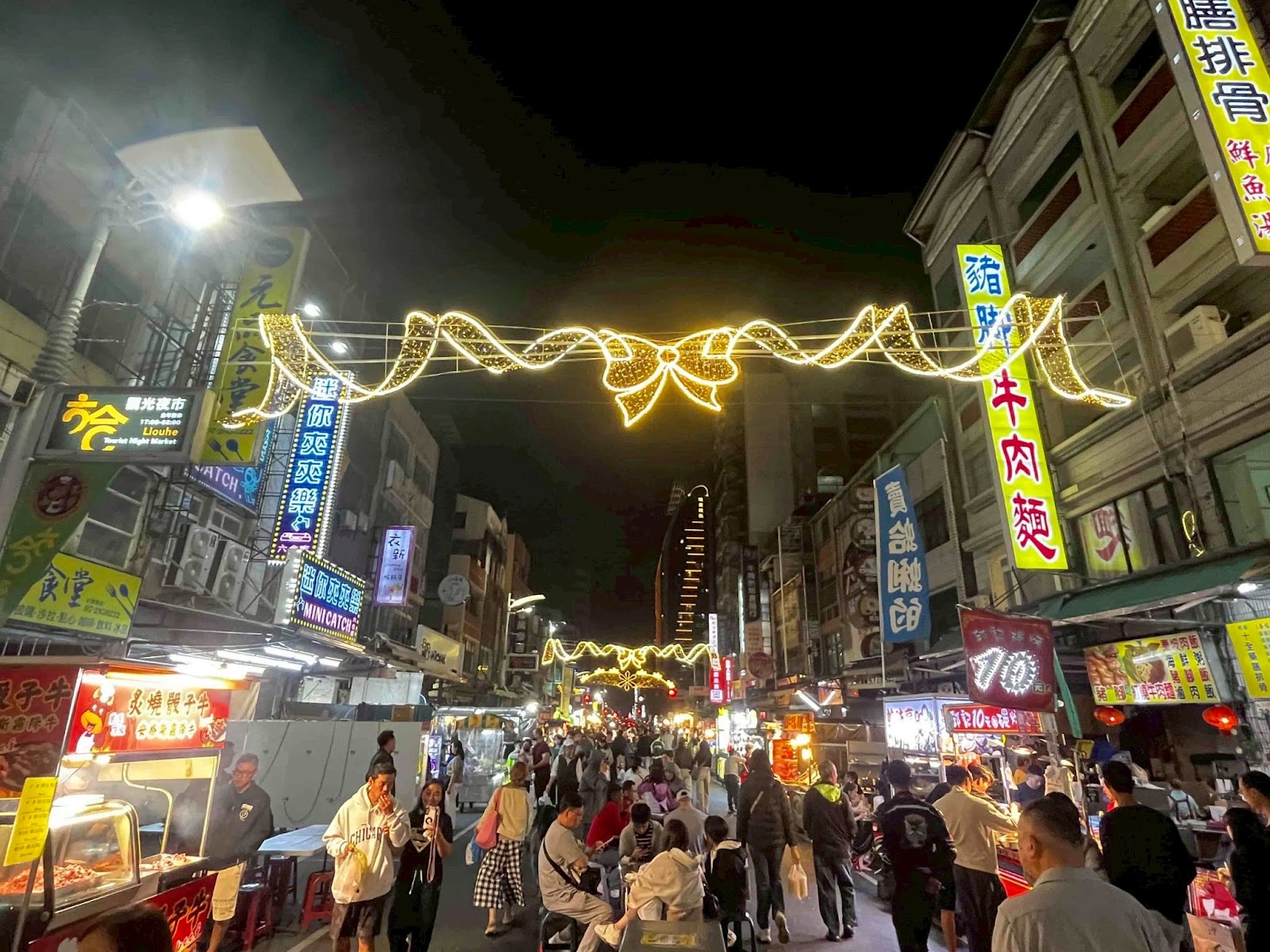 六合夜市街道夜間燈飾，人潮熙攘，兩側攤販林立