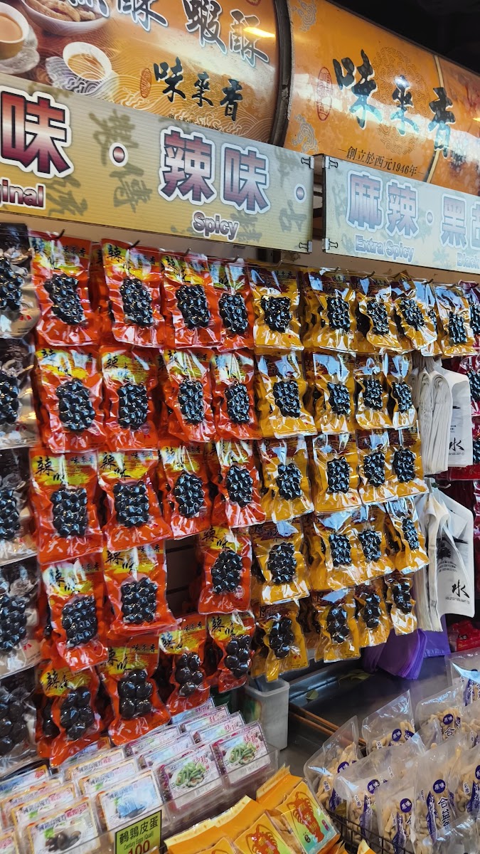 淡水老街零食店展示架，滿牆的黑色醃製零食包裝，標示原味、辣味、麻辣味