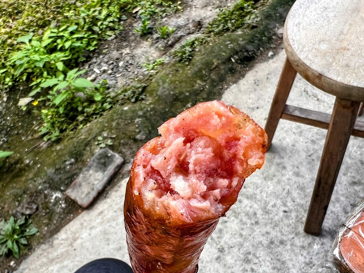 手持已咬一口的馬告香腸，可見粉紅色飽滿肉質內餡