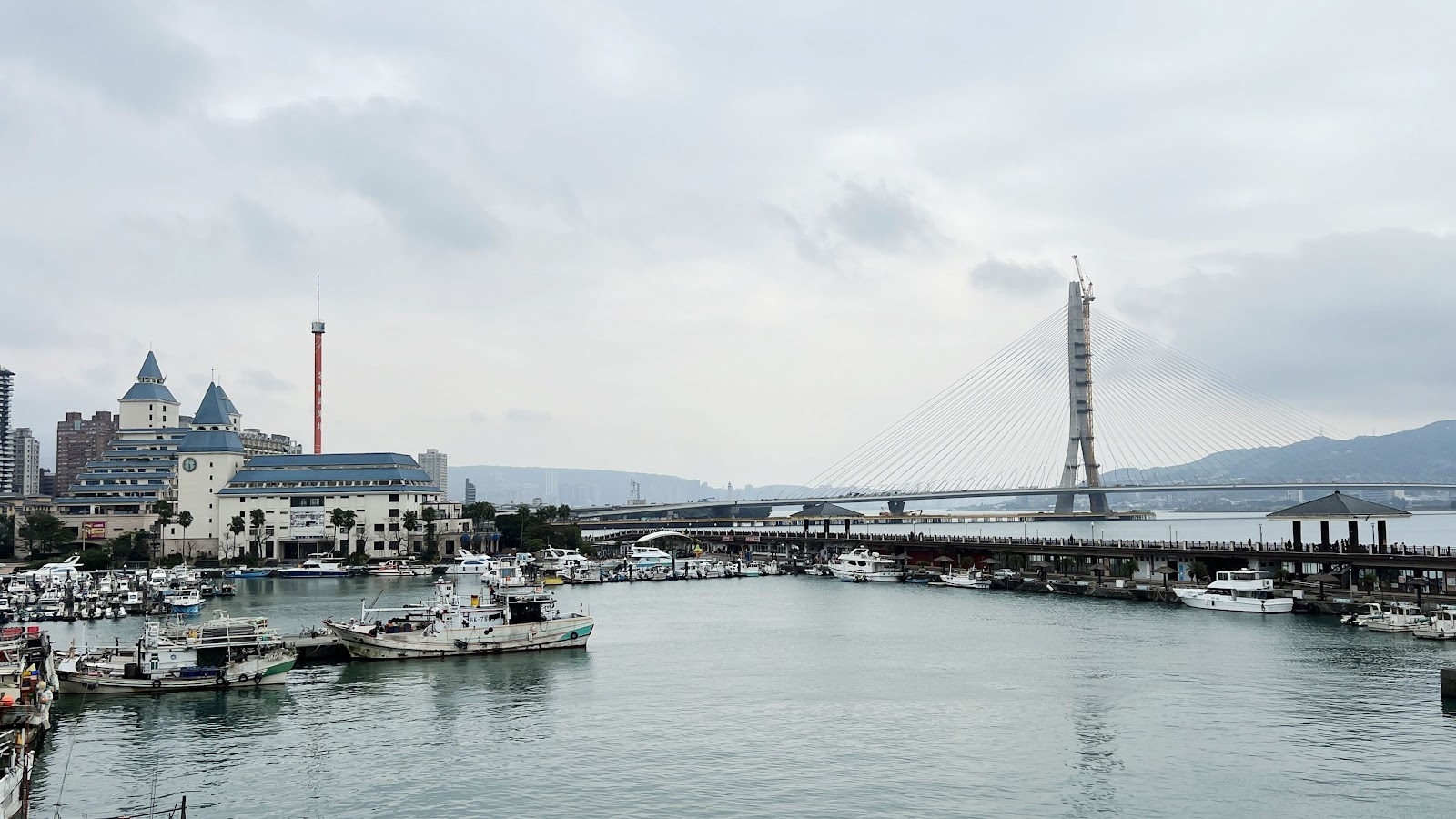 淡水漁人碼頭港區全景,左側歐式城堡建築,中央漁船停靠,右側情人橋遠景