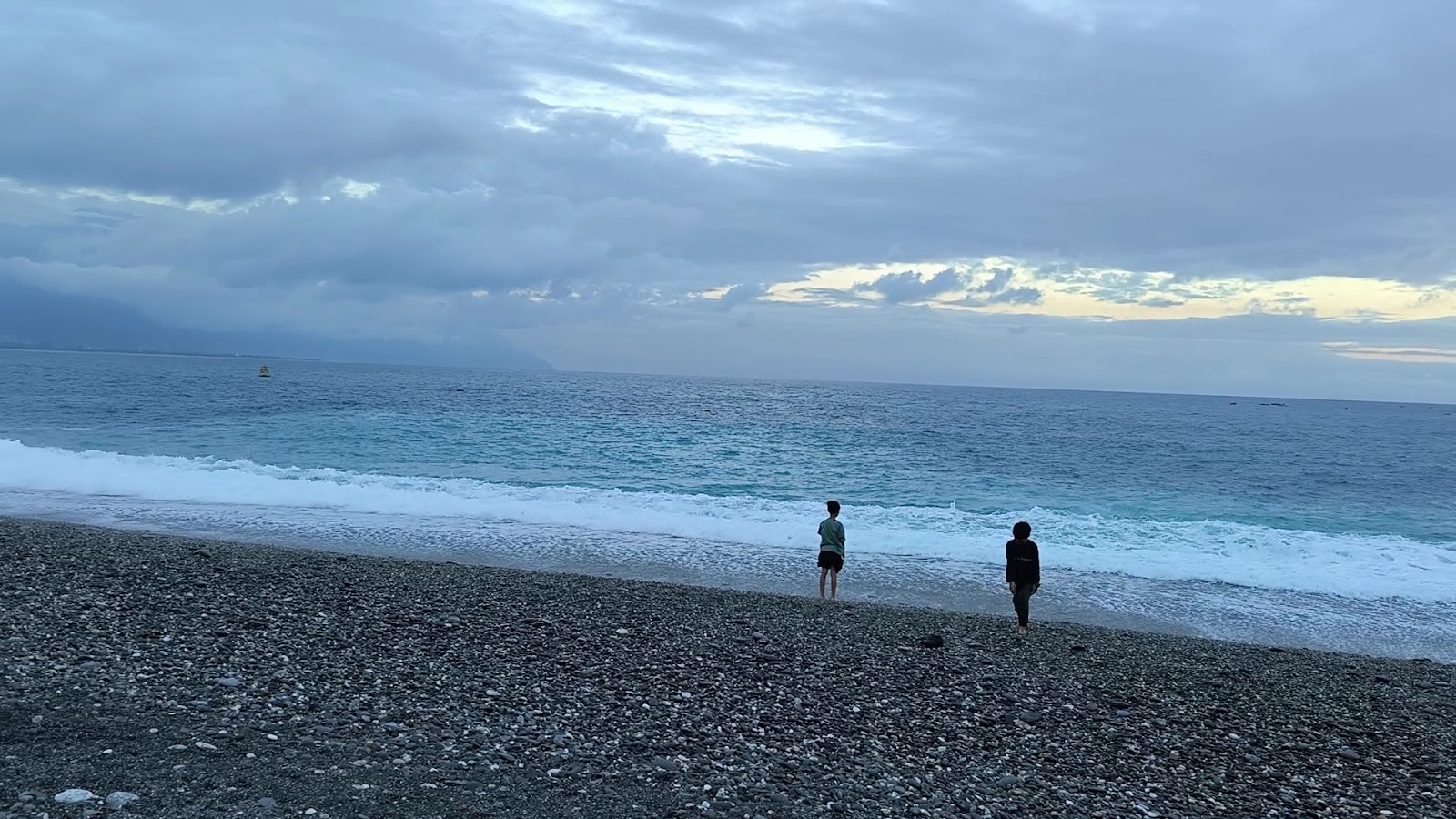七星潭礫石海灘黃昏，兩人背對站立望海，藍灰海面海浪拍打，暮色天空