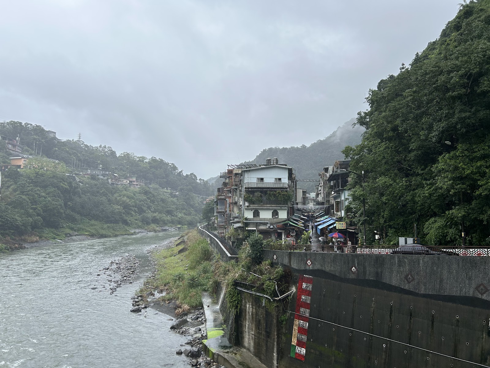 南勢溪河岸遠景，右側烏來老街建築依山而建，左側溪流蜿蜒，雲霧繚繞