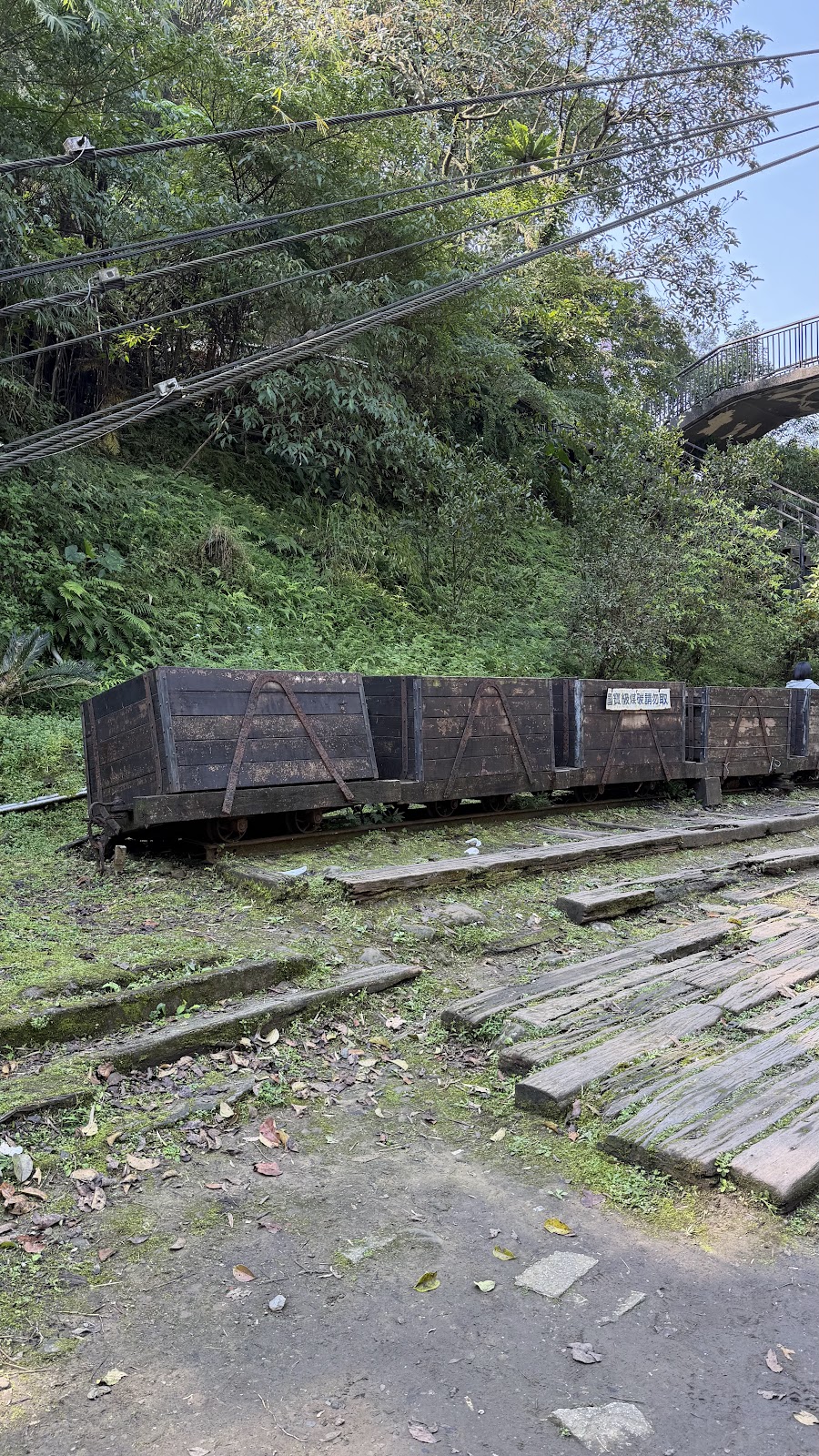 平溪廢棄礦車停放鐵軌，背景吊橋綠樹