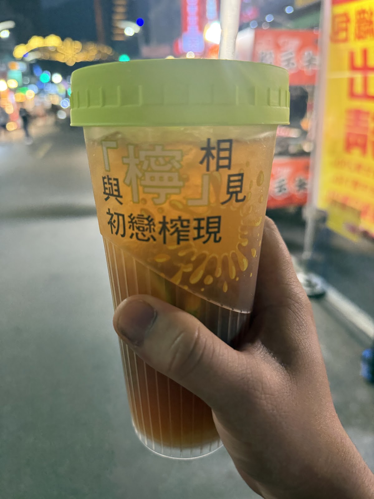 手持一杯與檸相見鮮榨檸檬茶飲料,背景是六合夜市霓虹燈光