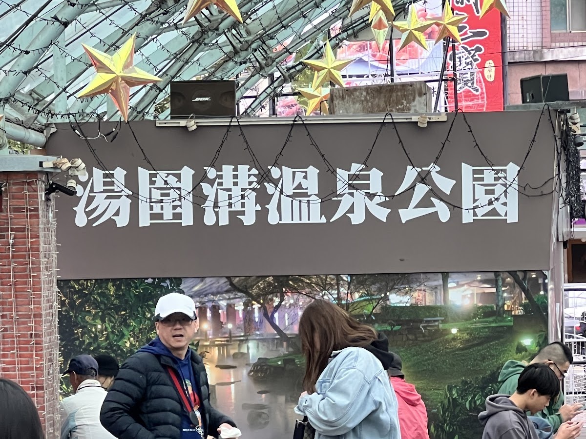 湯圍溝溫泉公園入口招牌，玻璃拱頂下遊客熙來攘往，金色星星裝飾