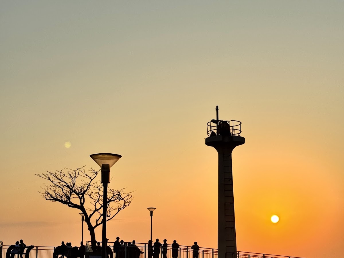 東石漁人碼頭夕陽剪影，燈塔與行人映襯橘紅天空海景
