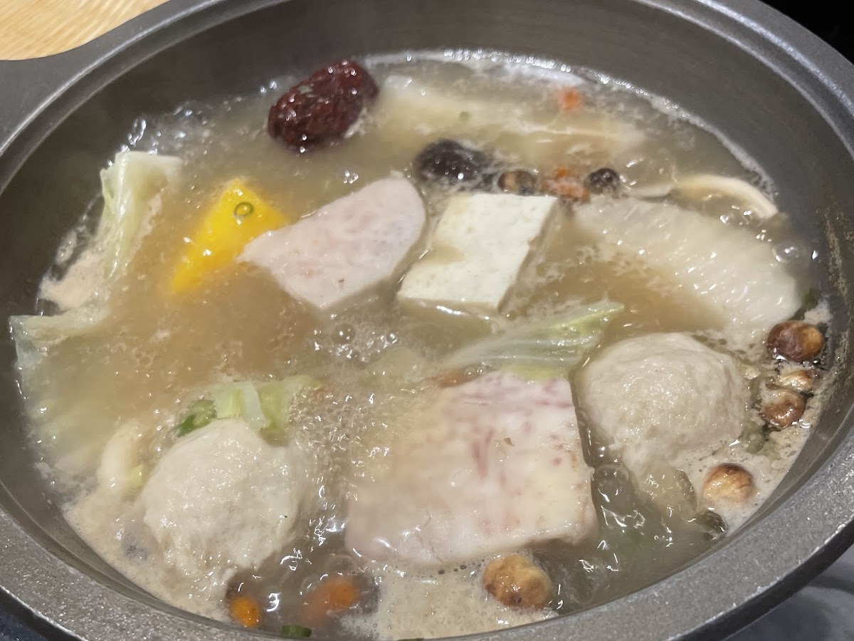 誠石火鍋岡山店鍋中丸子豆腐蔬菜在清澈湯底中沸騰，旁邊有紅棗食材