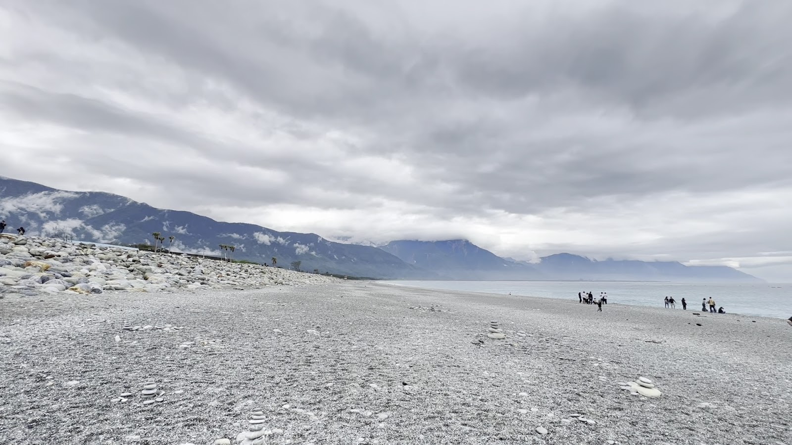 七星潭礫石海灘全景，中央山脈雲霧環繞，遊客在礫石灘散步