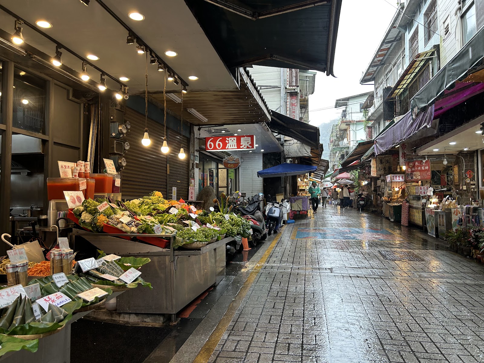 烏來老街街道雨天景色，蔬菜攤與66溫泉招牌兩側店家