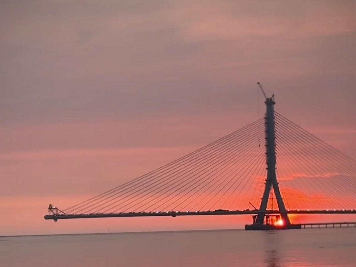 情人橋黃昏剪影,橙紅色夕陽天空,橋身與纜索輪廓清晰,水面平靜倒影