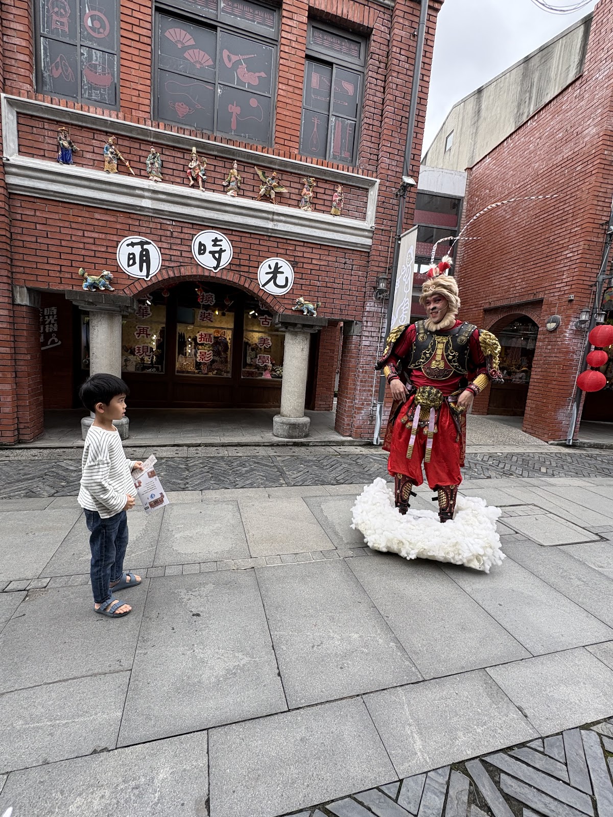 宜蘭傳藝園區內小孩好奇地面對傳統武將偶人，萌時光店家紅磚建築背景