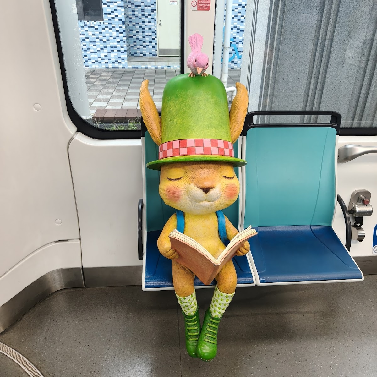 淡水輕軌車廂內可愛松鼠公仔坐在座位上閱讀,頭戴綠色帽子