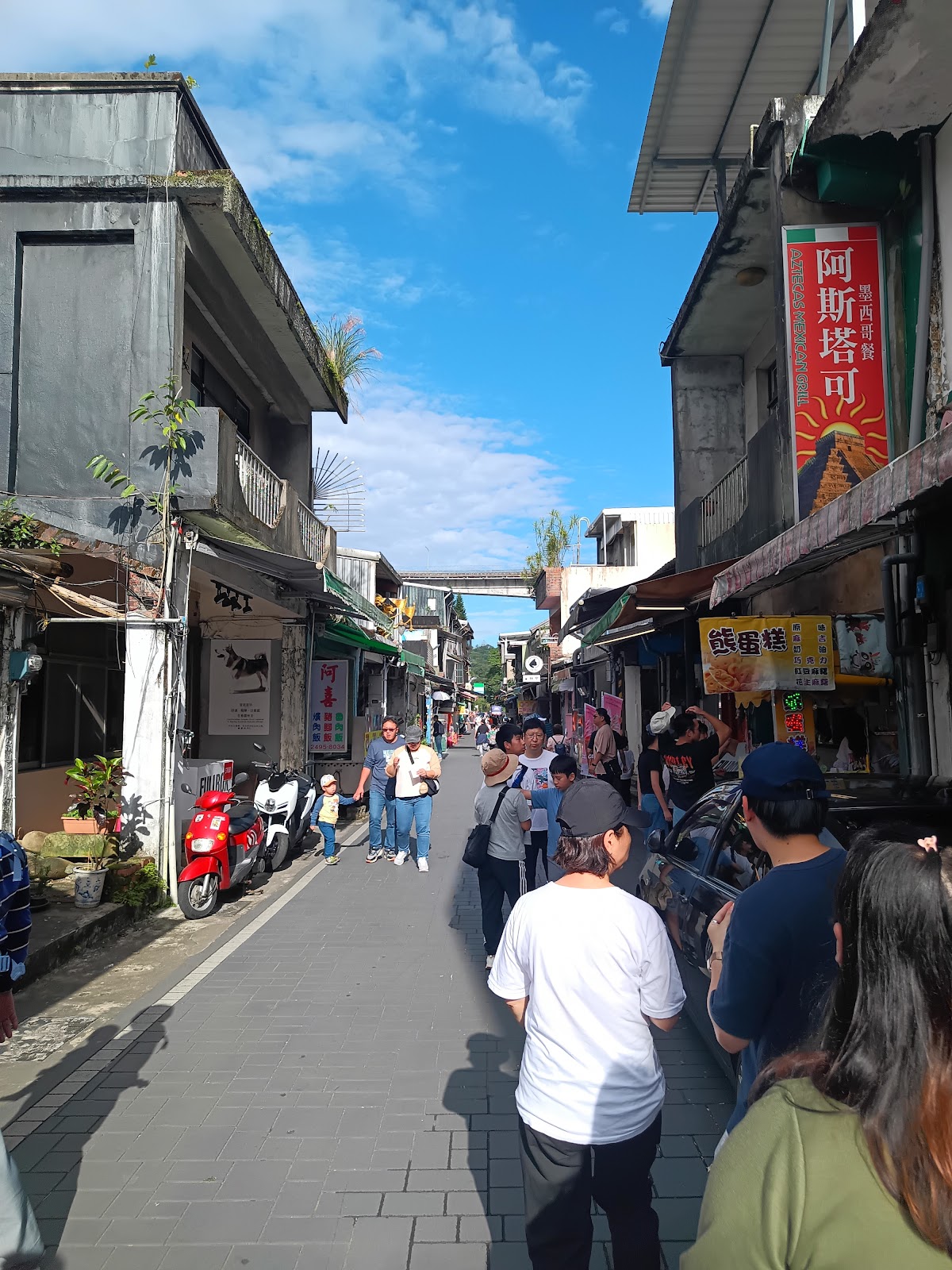 十分老街街巷內遊客漫步，兩側老建築商店，藍天白雲