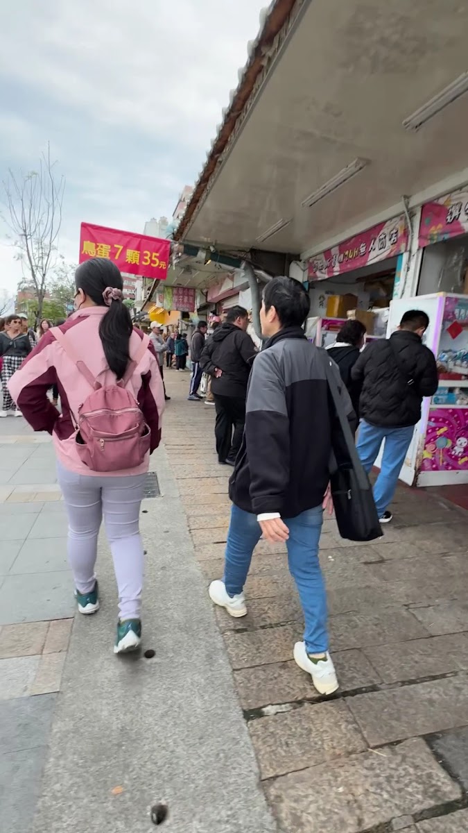 淡水老街商店街，遊客成群走動，兩側掛著紅色旗幟和各式招牌