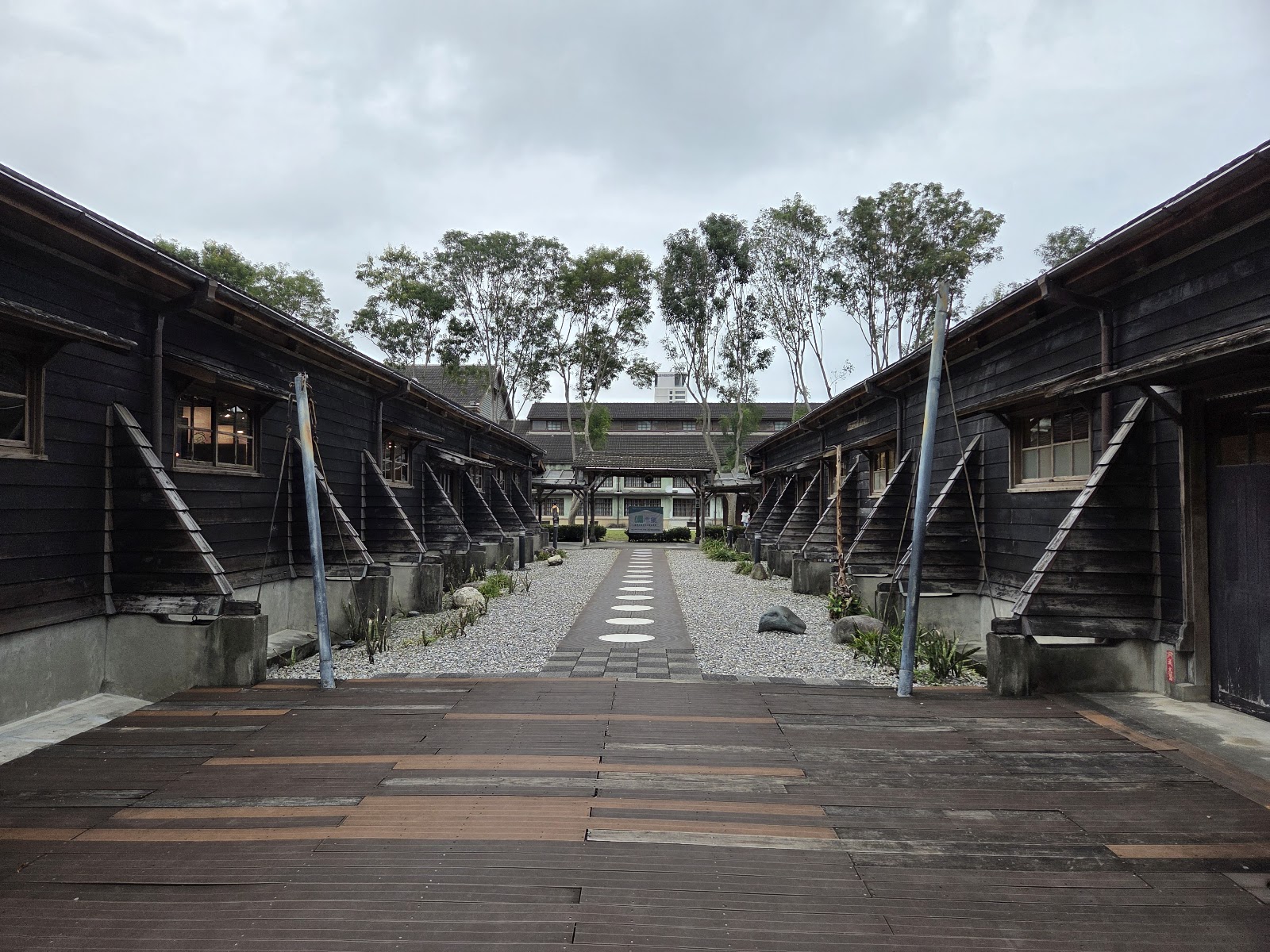 花蓮文創產業園區日式木造黑色建築對稱長廊，礫石步道延伸，遠處綠樹
