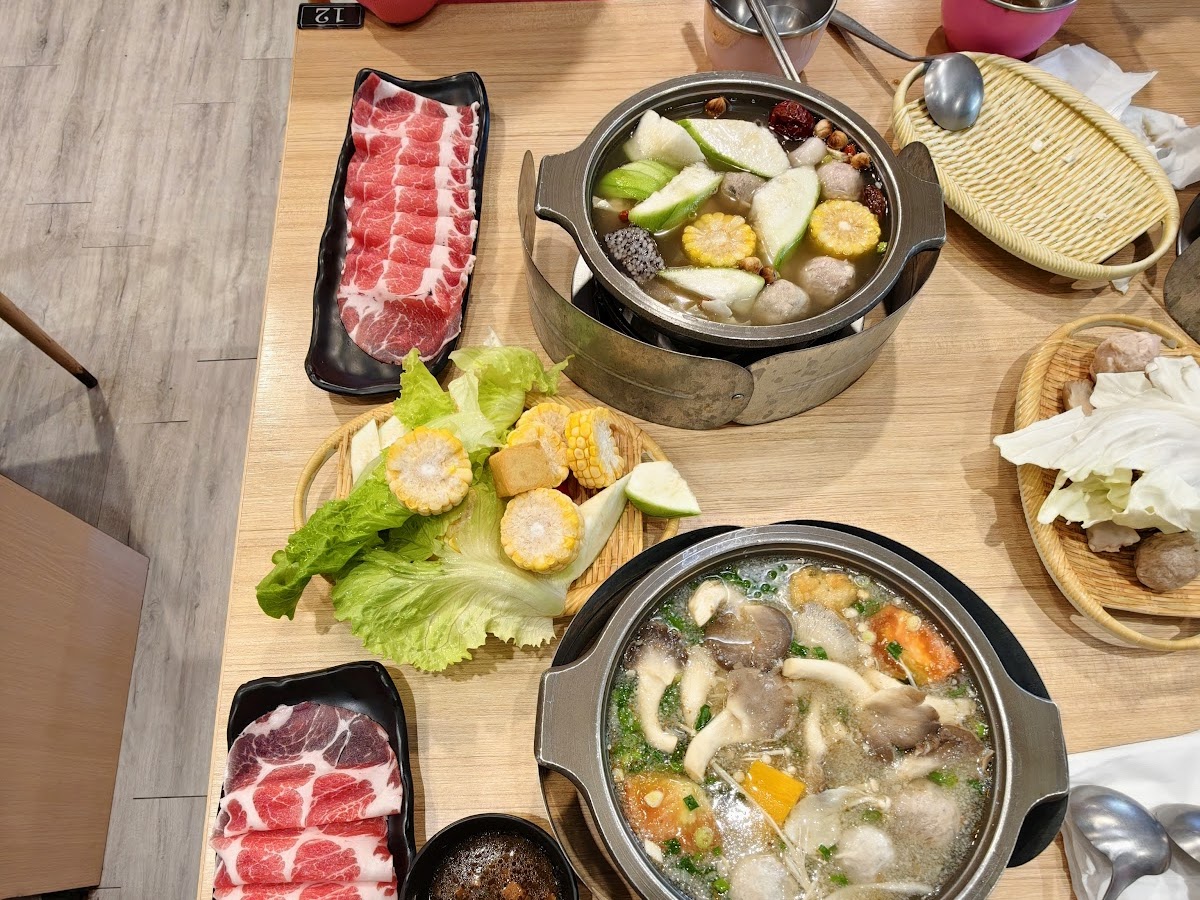 誠石火鍋岡山店桌面俯視，兩個火鍋鍋底並排，旁邊有薄切牛肉片和各種蔬菜