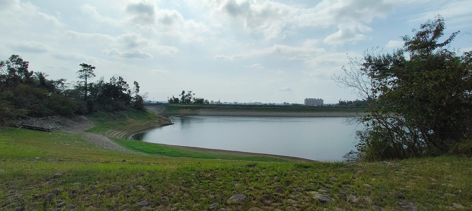 蘭潭水庫全景，湖岸草地礫石遠眺嘉義市區