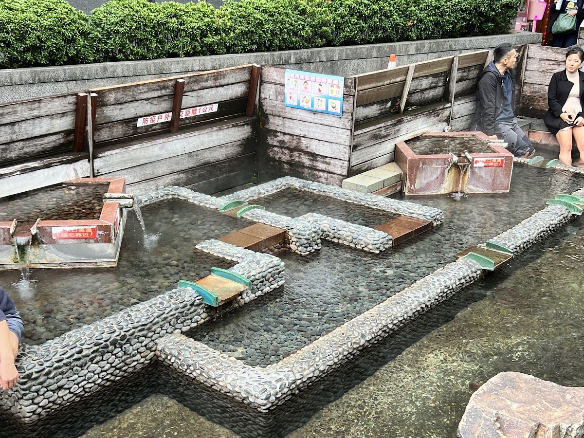 湯圍溝溫泉公園戶外石砌泡腳池，溫泉水清澈，遊客坐在木椅上放鬆泡腳