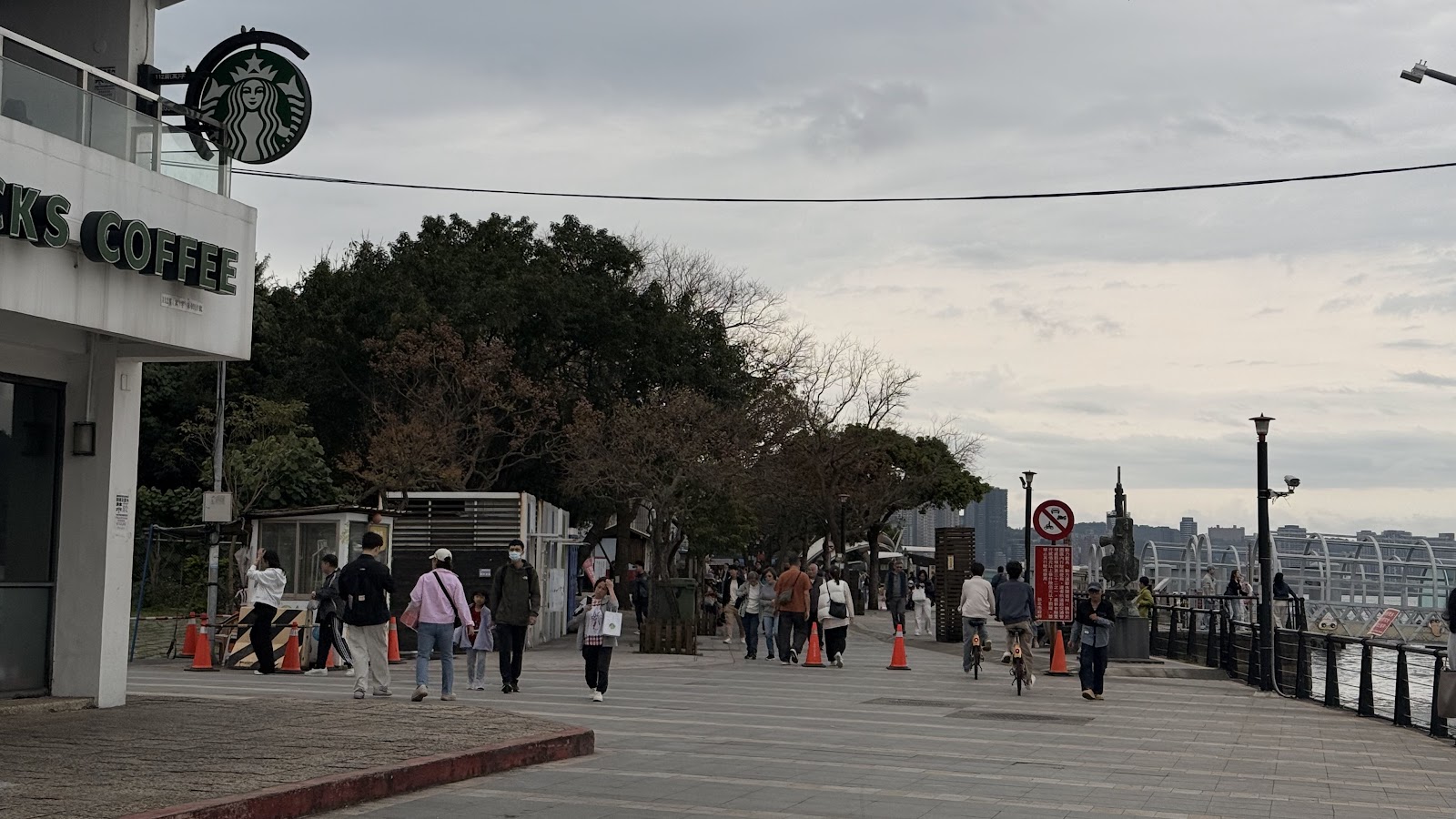 淡水老街河岸步道，左側星巴克咖啡招牌，遊客漫步