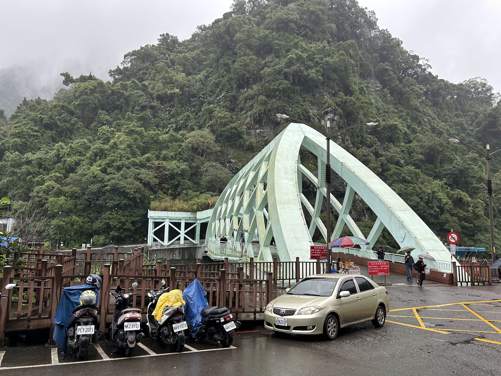 烏來吊橋淺綠色鋼架正面全景，背景雲霧繚繞山頭，雨天氣氛