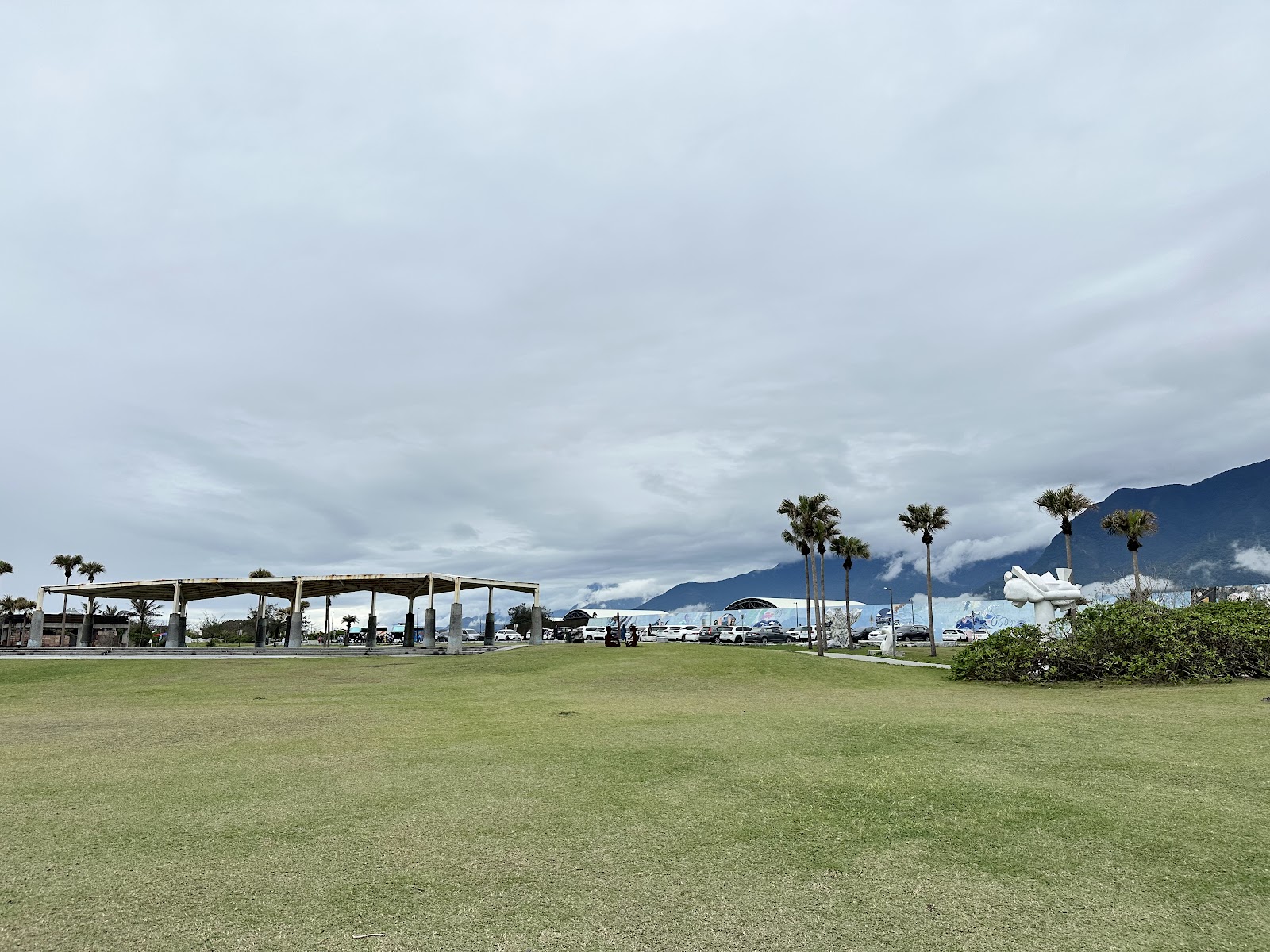 七星潭海濱公園草地廣場，涼亭遮蔭，棕櫚樹環繞，背景中央山脈