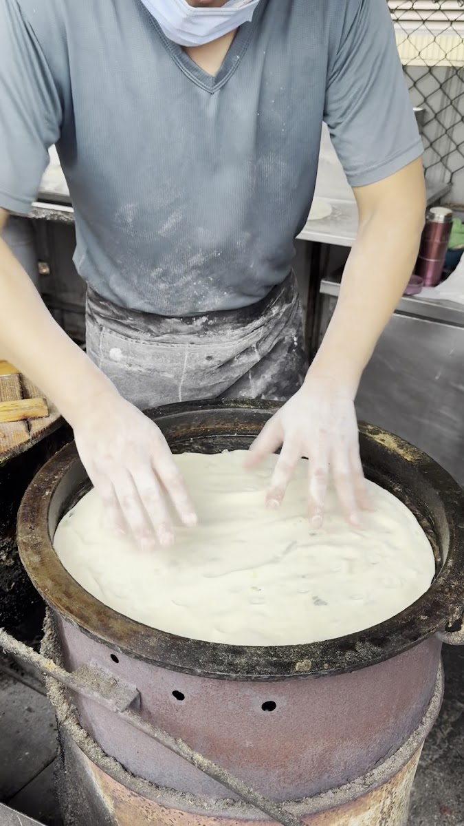 宜蘭無名蔥油餅師傅雙手壓麵團於炭爐上