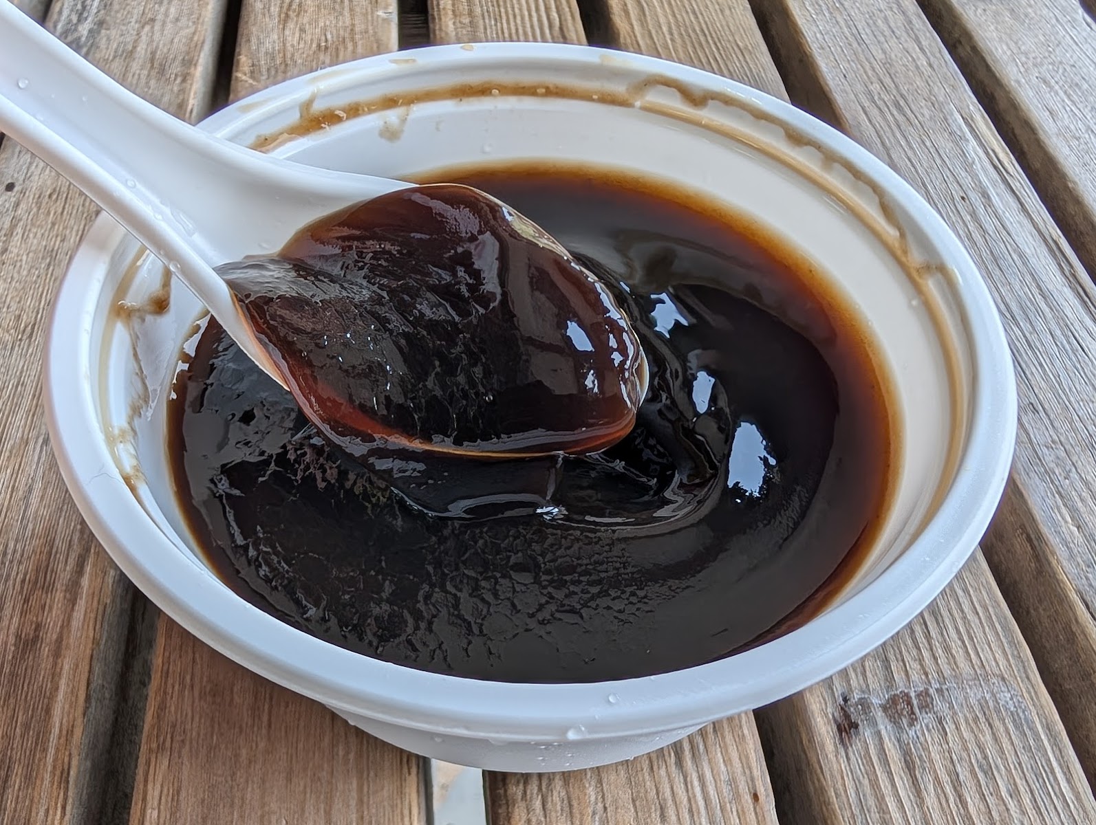 仙草龍仙草原汁近拍，濃稠深黑色仙草裝在白碗中，湯匙舀起一塊