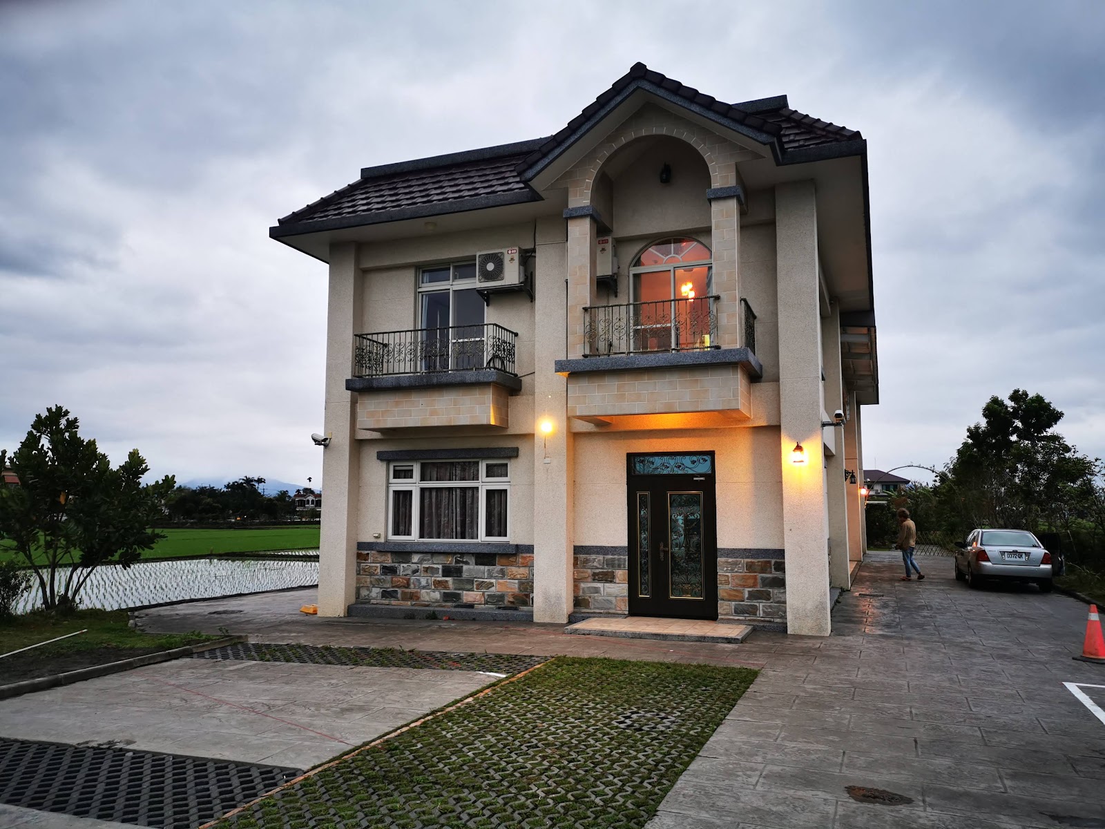 蘭天民宿黃昏歐式別墅外觀，米色石材建築，鐵藝陽台，前方石板路，左側稻田